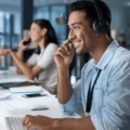 Support agent wearing a headset at a computer in a bright open-plan office.