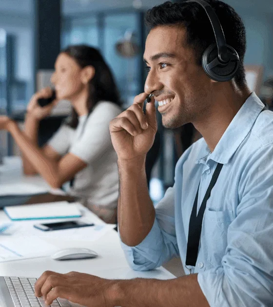 Support agent wearing a headset at a computer in a bright open-plan office.