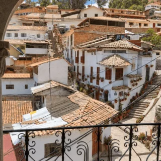 View of a hillside village with white houses and red-tiled roofs, framed by a stone archway and decorative iron railing.