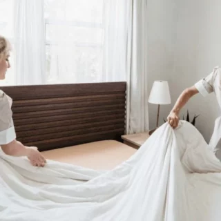 Two nurses straighten a bed with white sheets in a bright hospital room; UNIFOCUS logo visible in the top-left corner.