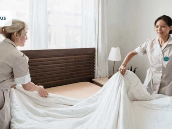 Two nurses straighten a bed with white sheets in a bright hospital room; UNIFOCUS logo visible in the top-left corner.