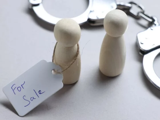 Two wooden peg dolls with a 'For Sale' tag, beside a pair of metal handcuffs in the background.