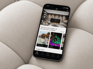 Smartphone resting on a beige sofa displaying a hotel app interface with featured images and an Explore More section.