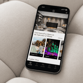 Smartphone resting on a beige sofa displaying a hotel app interface with featured images and an Explore More section.