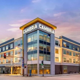 Corner view of a modern three-story office building with glass walls at sunset; CAMBRIA CAMBRIA sign on the top.