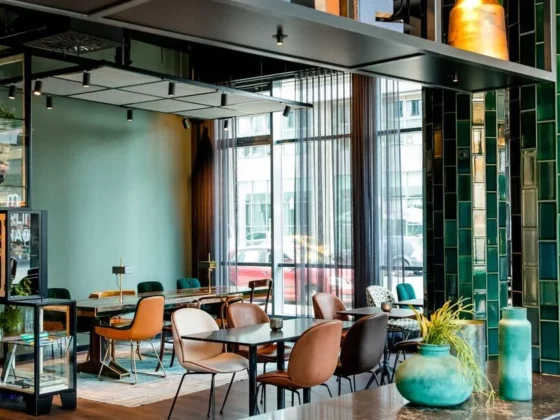 A stylish, modern cafe interior with teal-green tiled columns, mixed chairs, and large windows letting in daylight.