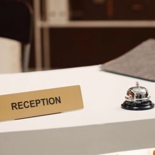 Reception desk with a gold sign reading 'RECEPTION' and a silver service bell on a white counter.