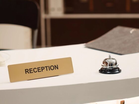 Reception desk with a gold sign reading 'RECEPTION' and a silver service bell on a white counter.