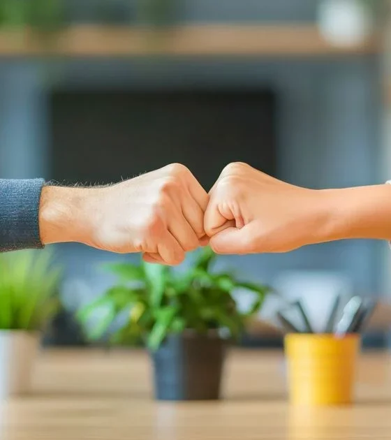 Two people fist-bumping over a desk in an office, signaling teamwork and agreement in a collaborative workspace