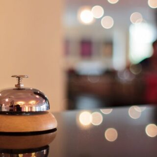 Polished hotel reception bell on a wooden base, resting on a glossy counter with warm, blurred lobby lights in the background.