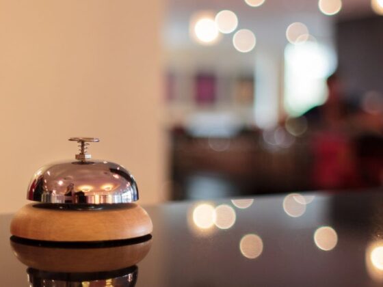 Polished hotel reception bell on a wooden base, resting on a glossy counter with warm, blurred lobby lights in the background.
