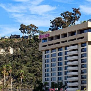 Sheraton hotel building on a hillside against a blue sky, with palm trees in the foreground.