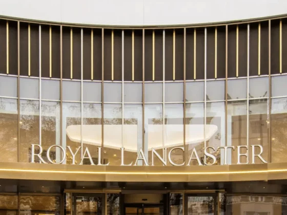 Front entrance of the Royal Lancaster hotel with a curved glass facade and gold accents surrounding the sign 'ROYAL LANCASTER'