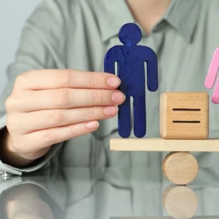 Blue male and pink female figures balanced on a wooden scale, symbolizing gender equality.