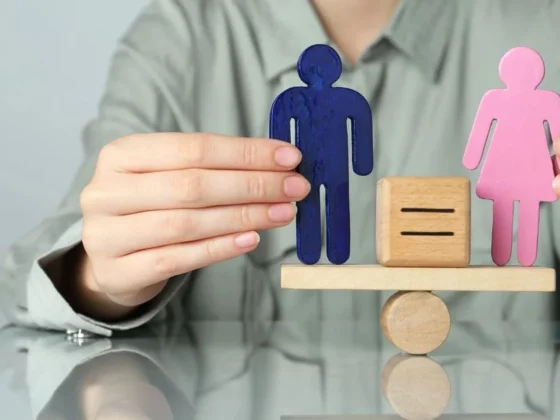 Blue male and pink female figures balanced on a wooden scale, symbolizing gender equality.