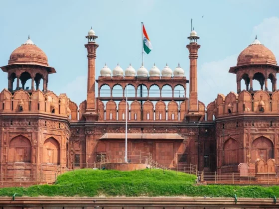 Red sandstone gateway with domed pavilions and multiple arches, topped by an Indian flag against a blue sky (historic monument copy)