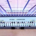 Row of people standing behind white podiums on a large stage at a conference, with a blue-lit ceiling and Chinese text on the backdrop.