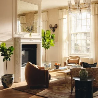 Bright living room with a white marble fireplace, large windows, and seating around a wooden coffee table.