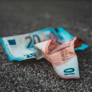 Crumbled euro banknotes lying on a rough asphalt surface on the ground as if dropped or discarded.