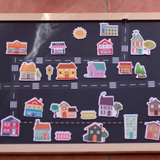Colorful sticker houses arranged on a chalkboard map with roads and a wooden frame.