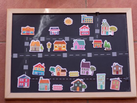 Colorful sticker houses arranged on a chalkboard map with roads and a wooden frame.