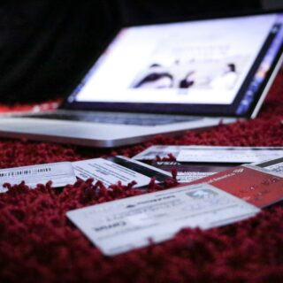 Laptop on a red carpet with scattered papers, cards, and tickets in the foreground (blurred screen).