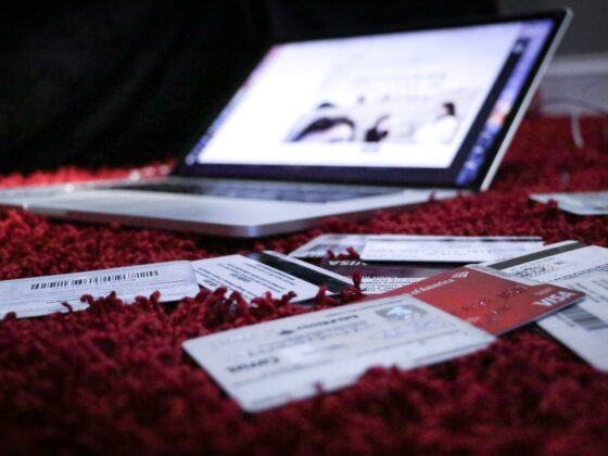 Laptop on a red carpet with scattered papers, cards, and tickets in the foreground (blurred screen).
