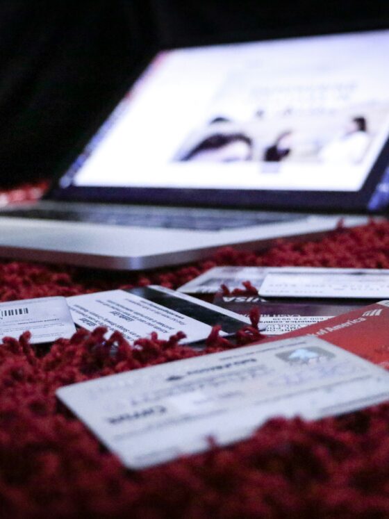 Laptop on a red carpet with scattered papers, cards, and tickets in the foreground (blurred screen).