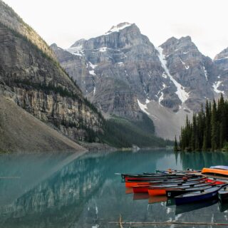 Turquoise alpine lake with colorful rowboats anchored at a rocky shore and towering snow-dusted mountains in the background