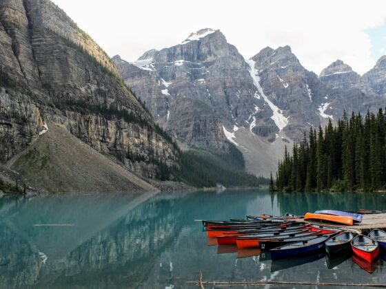 Turquoise alpine lake with colorful rowboats anchored at a rocky shore and towering snow-dusted mountains in the background