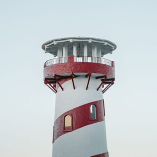 Red-and-white spiral striped lighthouse tower with a circular gallery and white lantern room against a pale blue sky.