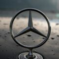 Close-up of a metal Mercedes-Benz emblem on a glossy, water-dotted car hood with a blurred background behind it.