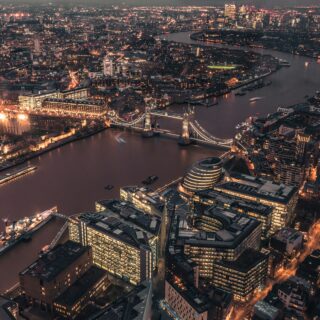 Aerial night view of central London with the Thames River and illuminated Tower Bridge across the water, city lights glowing around the skyline