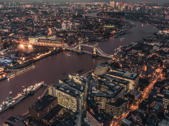 Aerial night view of central London with the Thames River and illuminated Tower Bridge across the water, city lights glowing around the skyline