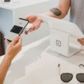 Person uses a smartphone to pay with Google Pay at a white checkout terminal, receipt in hand.