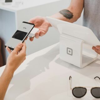 Person uses a smartphone to pay with Google Pay at a white checkout terminal, receipt in hand.