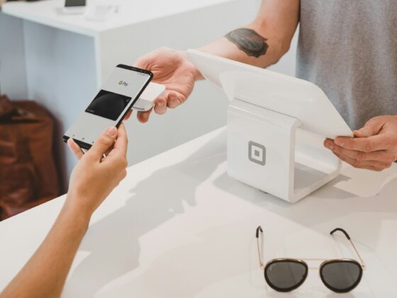 Person uses a smartphone to pay with Google Pay at a white checkout terminal, receipt in hand.