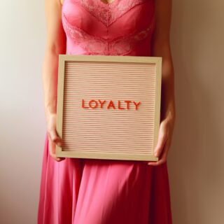 Person in a pink lace dress holding a small sign that reads LOYALTY.