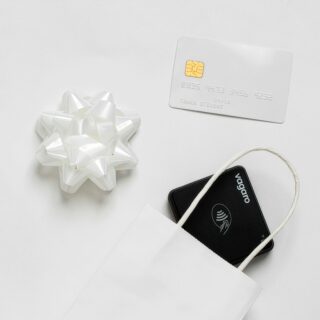 Close-up of a white gift bow beside a white EMV credit card with a gold chip on a pale background.