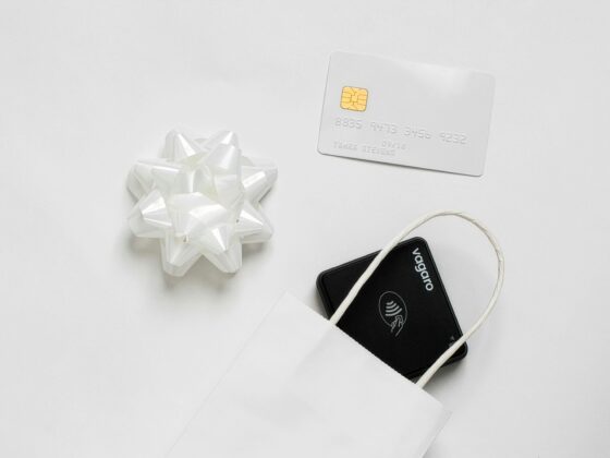 Close-up of a white gift bow beside a white EMV credit card with a gold chip on a pale background.