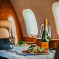 Luxurious airplane cabin dining table with a champagne bottle, two glasses, and a salad plate for two passengers.