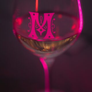 Close-up of a wine glass glowing with pink light and a decorative pink monogram on the bowl.