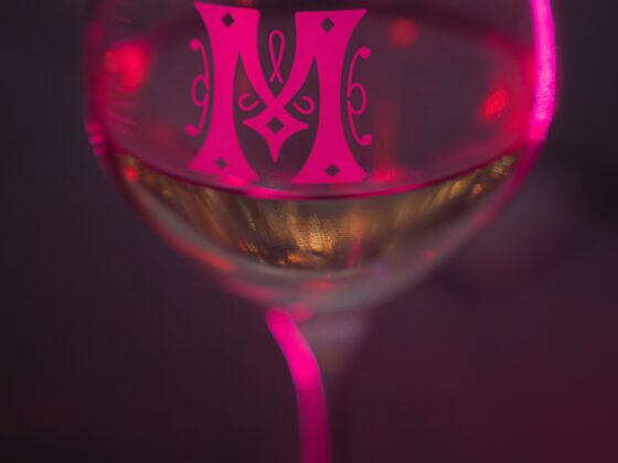 Close-up of a wine glass glowing with pink light and a decorative pink monogram on the bowl.