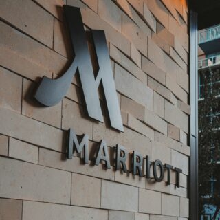 Exterior brick wall with large metallic Marriott logo and the word MARRIOTT beneath it, indicating a hotel entrance.