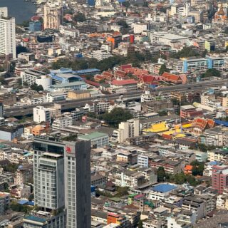 Aerial view of a dense city with a river on the left and a cluster of red-roofed temples near the bottom center.