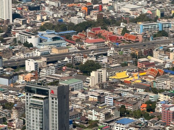 Aerial view of a dense city with a river on the left and a cluster of red-roofed temples near the bottom center.
