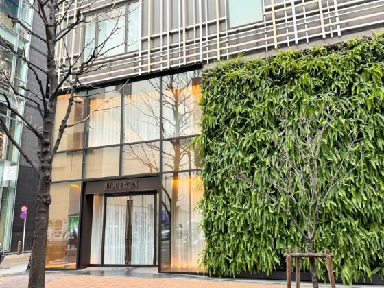 Modern glass storefront with 'EDITION' sign, large windows, and a dense green hedge along the right side of the entrance.