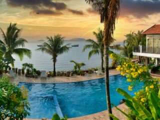 Tropical resort at sunset with an infinity pool, palm trees, and a seaside villa.
