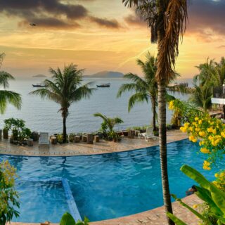 Tropical resort at sunset with an infinity pool, palm trees, and a seaside villa.