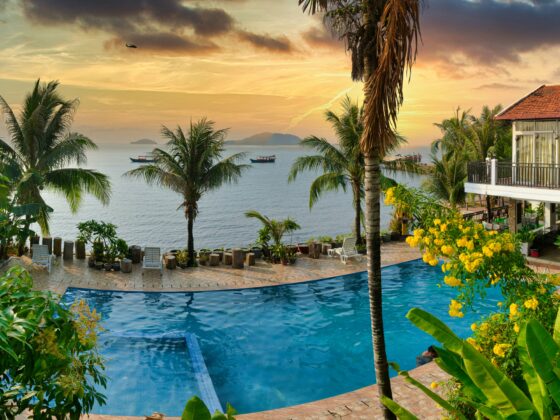 Tropical resort at sunset with an infinity pool, palm trees, and a seaside villa.